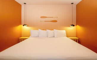 Una cama bien hecha con sábanas y almohadas blancas, dos mesitas de noche con lámparas, y un bate de madera colgado en la pared.