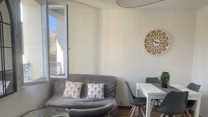 A modern living room with a grey sofa, two armchairs, a dining table with chairs, and a decorative wall piece.