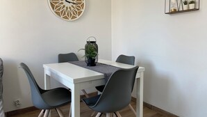 A dining area with a white table, four grey chairs, a decorative wall clock, and a plant in a lantern.