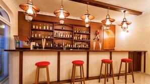 A bar area with wooden stools, a bar counter, and shelves stocked with bottles. - Alykes Park Bungalows & Apt (Zakynthos)