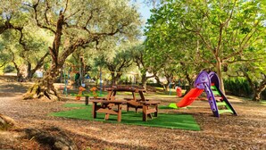 A park with picnic tables, a playground, and large trees. - Alykes Park Bungalows & Apt (Zakynthos)