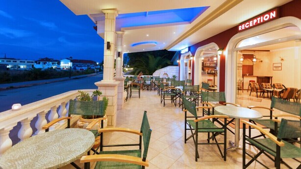An outdoor seating area with tables and chairs, a reception desk, and a view of the street. - Alykes Park Bungalows & Apt (Zakynthos)