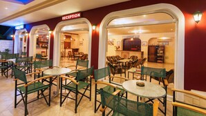 A reception area with a red wall and a sign, multiple tables and chairs, and a view into the interior. - Alykes Park Bungalows & Apt (Zakynthos)