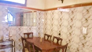 A dining area with a wooden table and chairs, a marble-patterned wall, and a small shelf with kitchen items. - Appart Boutchakkat 1 (Agadir)