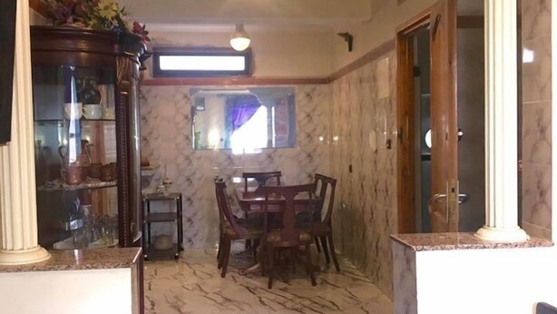 A living room with a marble floor, a dark leather sofa, a dining area with a wooden table and chairs, and a decorative cabinet. - Appart Boutchakkat 1 (Agadir)
