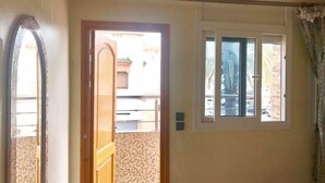 A room with a large mirror, a window with blinds, and a door leading to an outdoor area. - Appart Boutchakkat 1 (Agadir)
