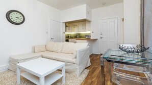 Ein modernes Wohnzimmer mit einem weißen Sofa, einem Glastisch und einer Küche im Hintergrund.