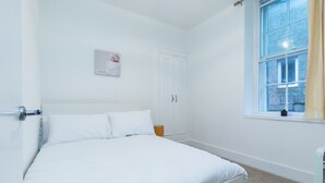 Ein Schlafzimmer in Weiß mit einem Bett, einem Kleiderschrank und einem Fenster mit Vorhängen.