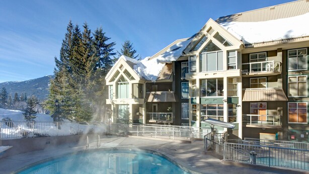 A hotel with a pool, snow-covered roofs, and a mountainous backdrop.