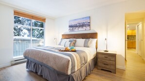 A bedroom with a large bed, a nightstand, a window with a view of a snowy landscape, and a painting above the bed.