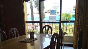 A dining area with a round wooden table and chairs, large windows with a view of buildings and trees, and a sign indicating a smoking area. - Callao Backpacker - Adults Only (Callao)