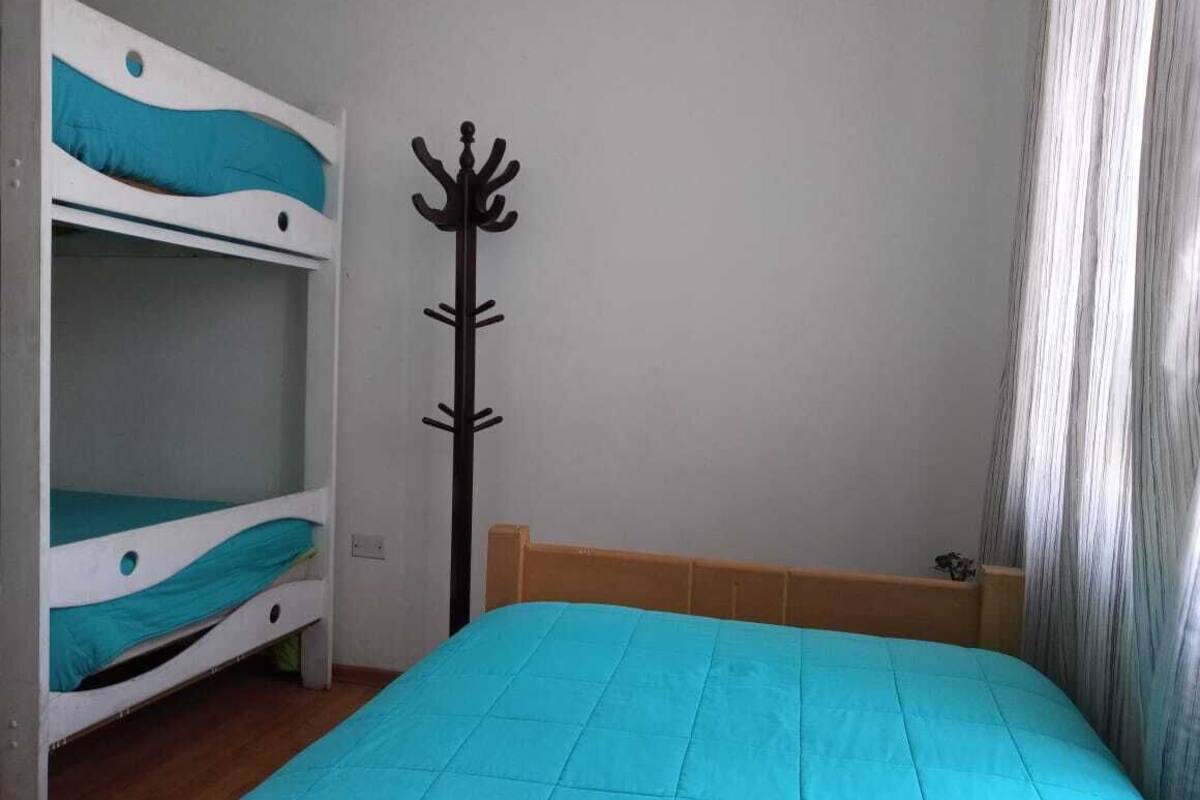 A bedroom with a bunk bed, a single bed, a coat rack, and a window with curtains.