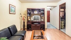 A living room with a black leather sofa, a wooden coffee table, a television on a wooden stand, and a framed picture on the wall. - Callao Backpacker - Adults Only (Callao)