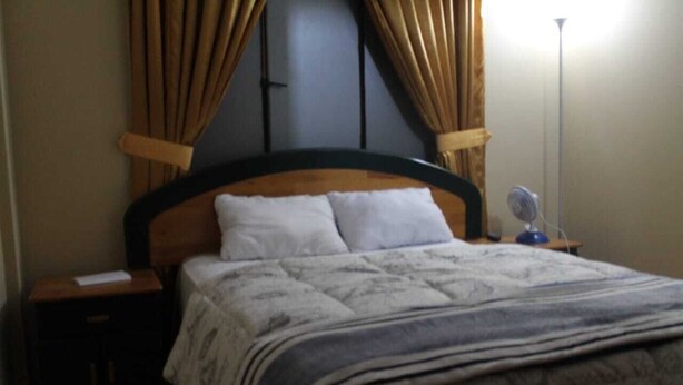 A neatly made bed with a wooden headboard, a bedside table with a lamp, and a nightstand. - Callao Backpacker - Adults Only (Callao)