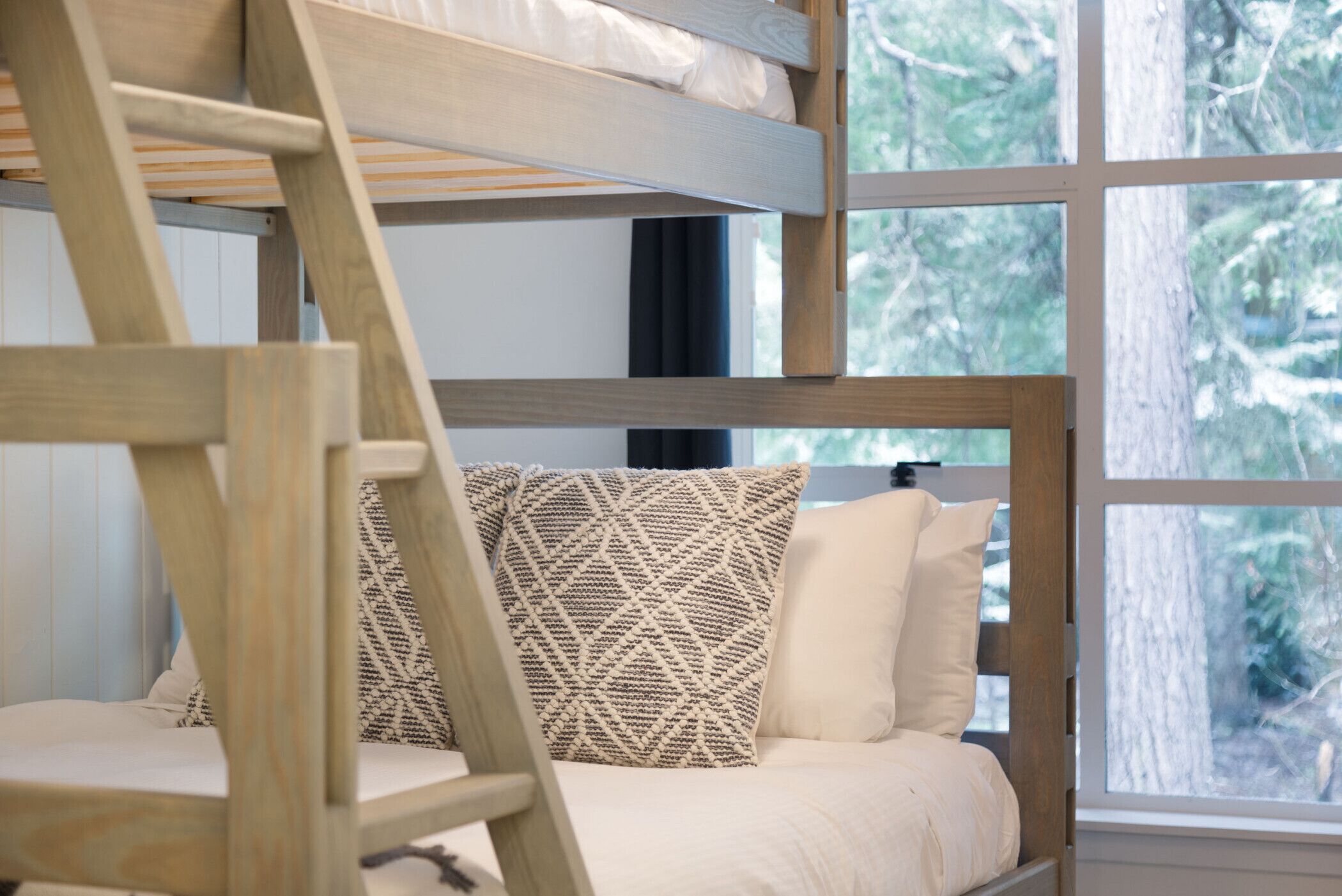 A bunk bed with a wooden ladder, a patterned pillow, and a white mattress.