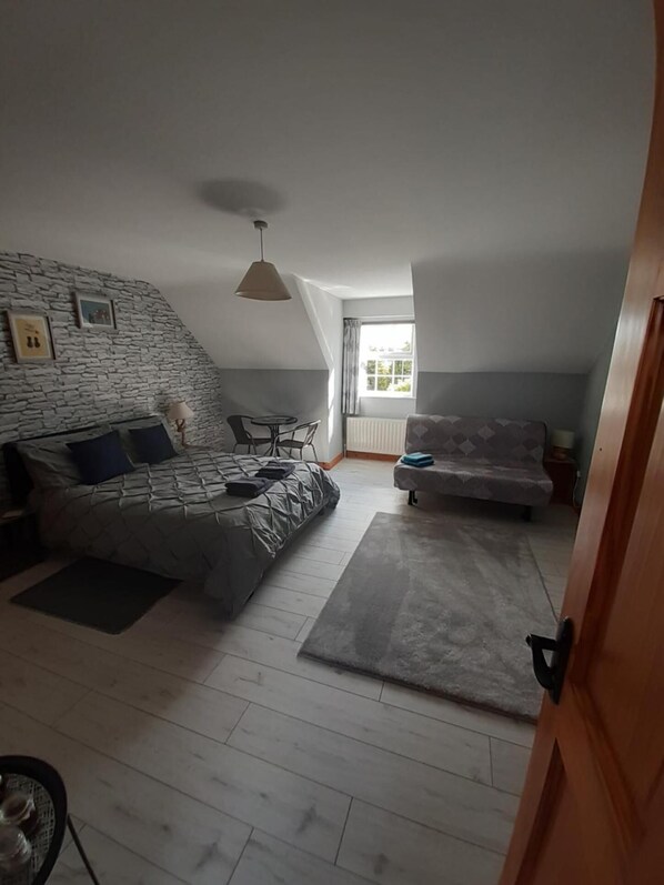 Quarto estilo loft com teto inclinado, uma cama, um sofá e uma mesa de jantar.