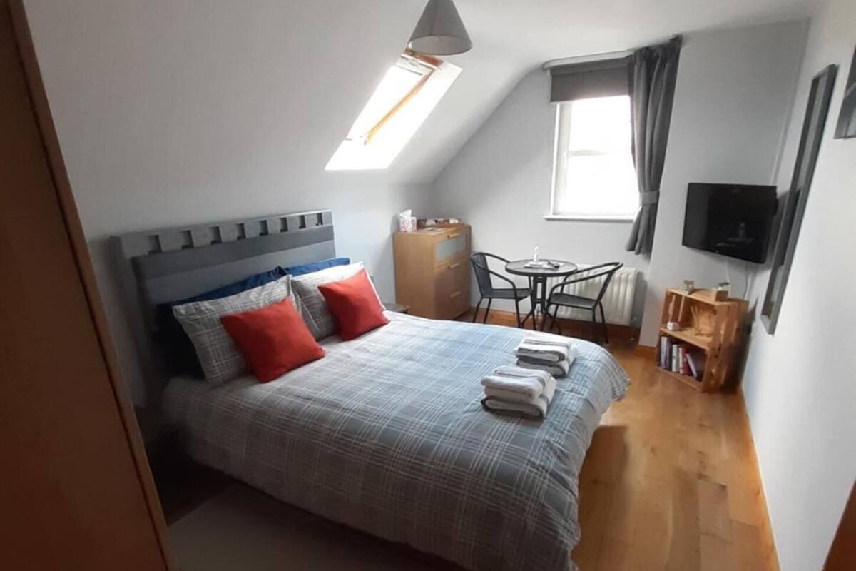 A bedroom with a bed, a desk, a chair, a TV, and a window.