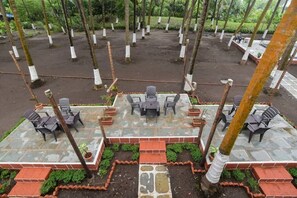 Un espace extérieur aménagé en terrasse, avec une bordure en briques, une table centrale entourée de chaises et des plantes en pot.