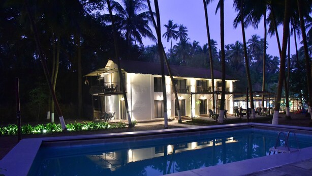 Ein Hotel mit Swimmingpool, umgeben von Palmen und einer gut beleuchteten Fassade.