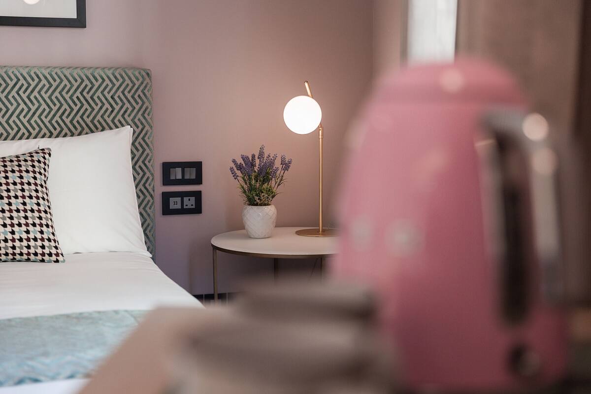 Un lit bien fait, agrémenté d’oreillers à motifs, une table de chevet avec une lampe et une plante en pot.