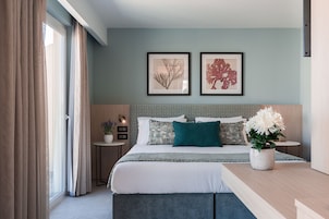 A modern bedroom with a large bed, a nightstand, a potted plant, and two framed pictures on the wall.