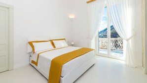 A bedroom with a bed, white walls, a window with curtains, and a view of a balcony. - Private Villa with Jacuzzi, Terraces, Sea View and Breakfast (Amalfi)