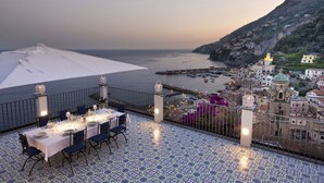 A terrace with a table set for dining, overlooking a coastal town and the sea. - Private Villa with Jacuzzi, Terraces, Sea View and Breakfast (Amalfi)