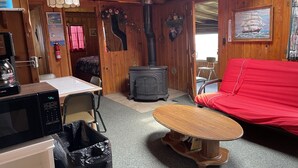 Een gezellig interieur van een blokhut met een houten tafel, een rode bank, een fornuis en een koffiezetapparaat.