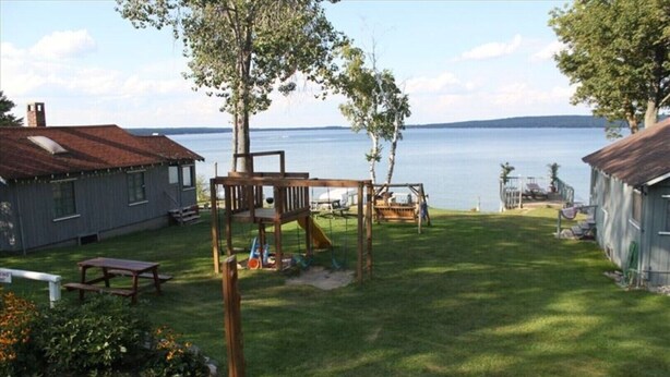Een achtertuin met een houten schommel, een picknicktafel en uitzicht op een meer.