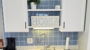 A kitchen with white cabinets, a double sink, a coffee maker, and a decorative 'HOME' sign above the sink.