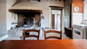 A rustic kitchen with a wood-burning stove, a dining table, chairs, and a refrigerator. - Secluded location and absolute tranquility in Tuscany (Monticello Amiata)