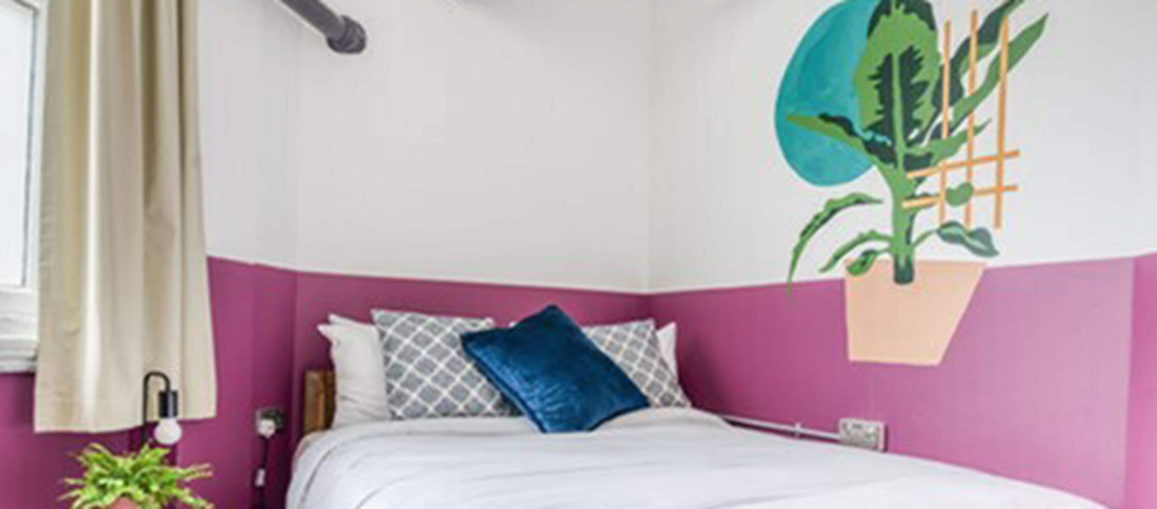 A bedroom with a bed, pillows, a nightstand, a lamp, and a wall-mounted plant.