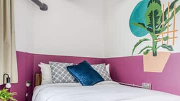 A bedroom with a bed, pillows, a nightstand, a lamp, and a wall-mounted plant.