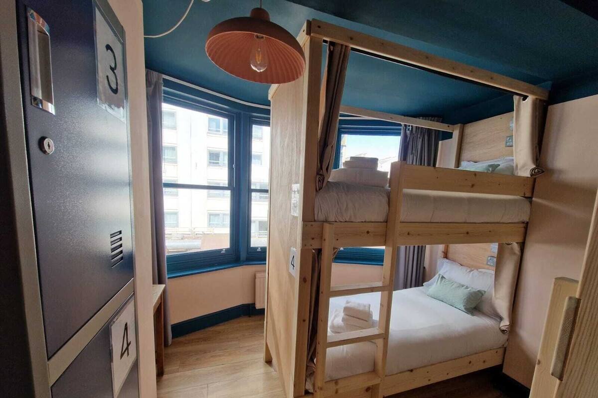A bunk bed room with a window, a door with a number, and a ceiling light.
