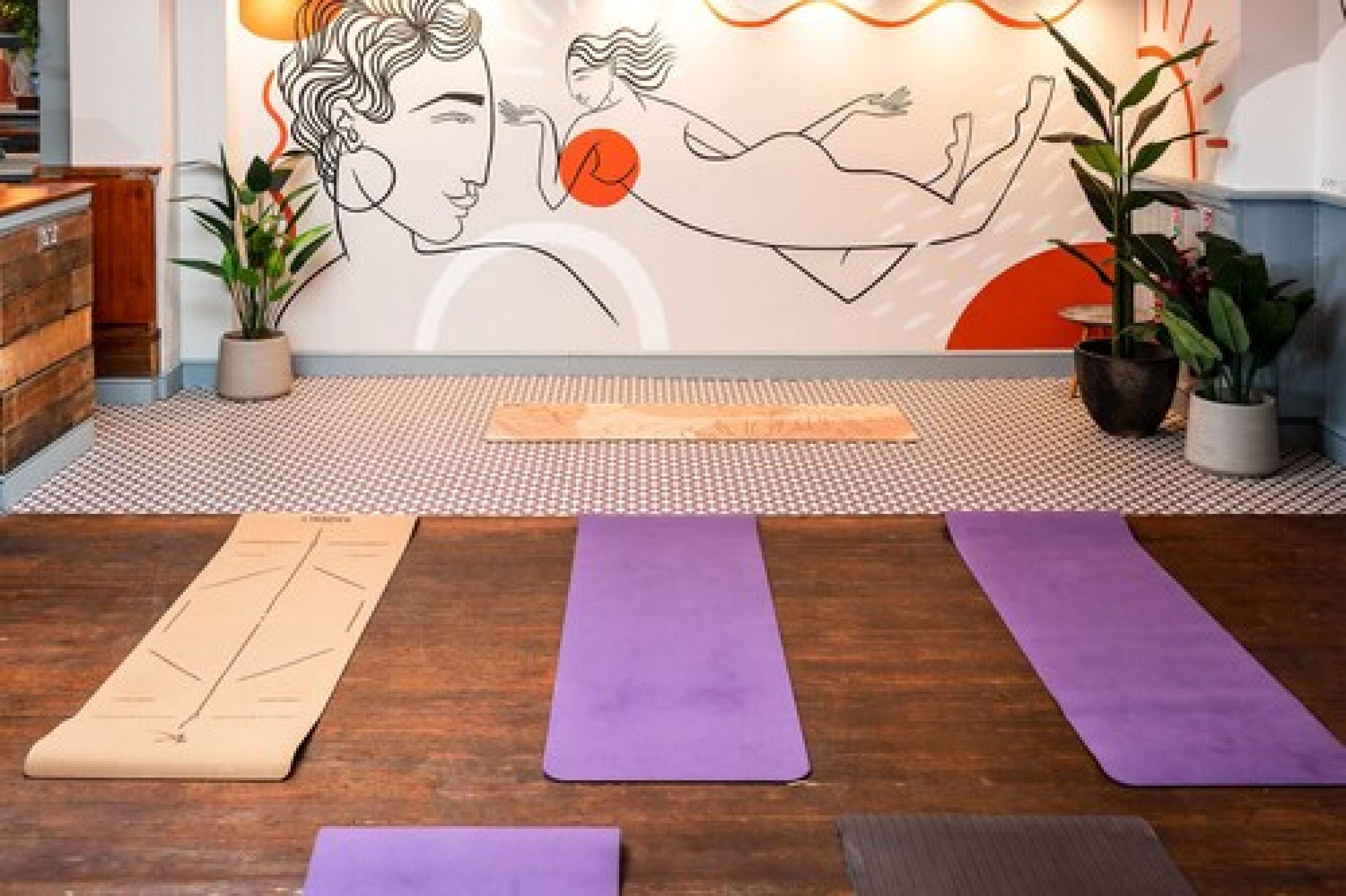 Un estudio de yoga con suelo de madera, un tapete estampado y tres colchonetas de yoga.