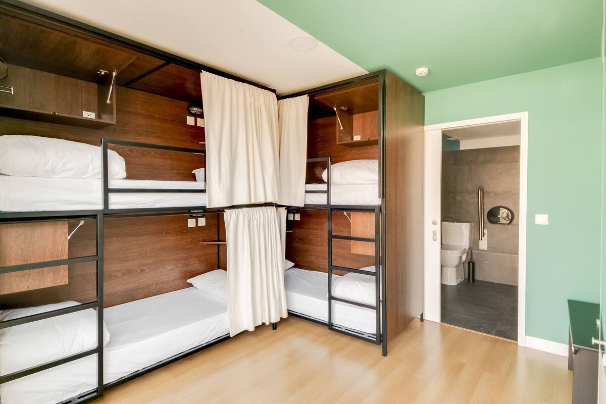 A room with bunk beds, a wooden ceiling, a door leading to a bathroom, and a green wall.