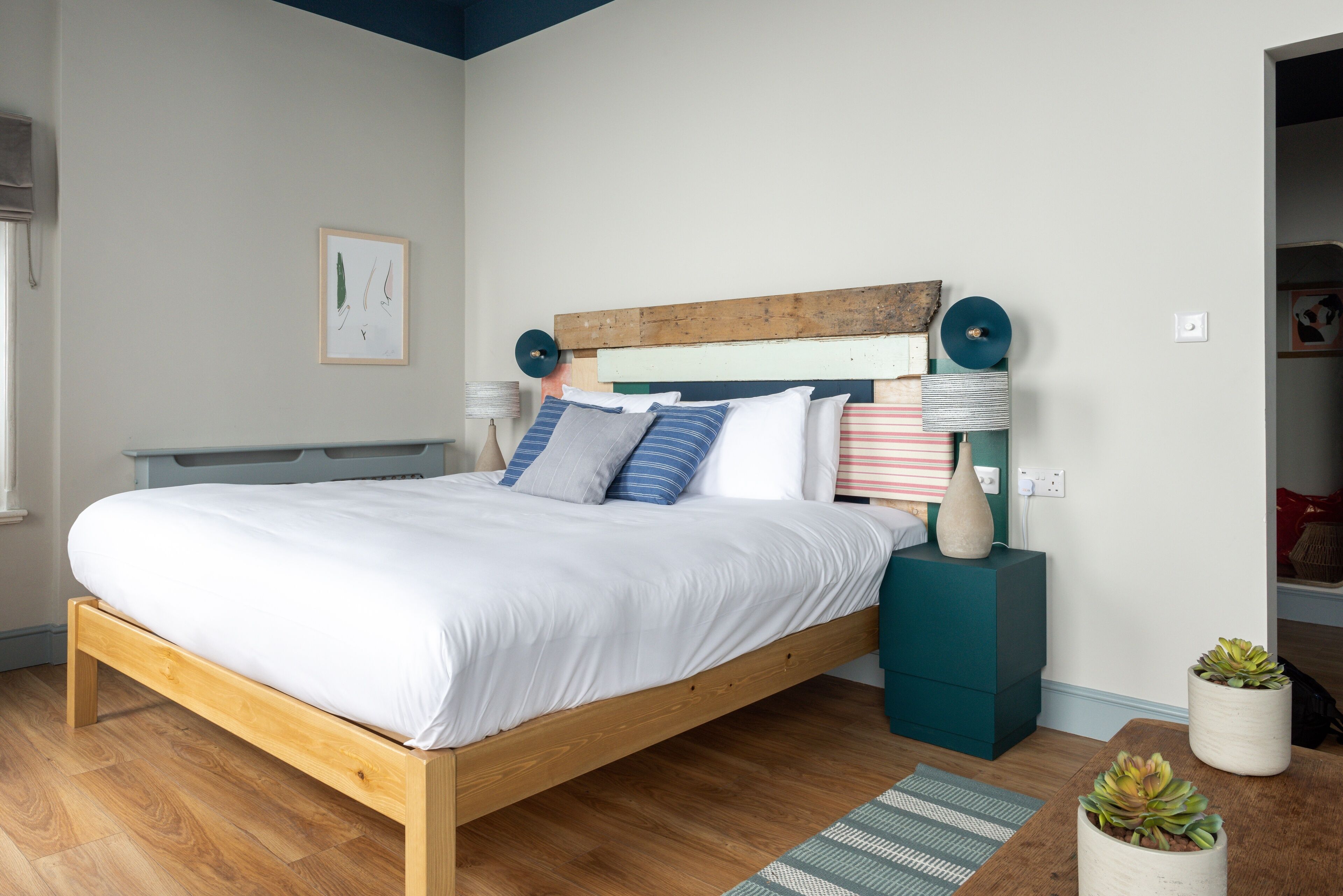 A modern bedroom with a wooden bed, teal nightstands, and a small potted plant.