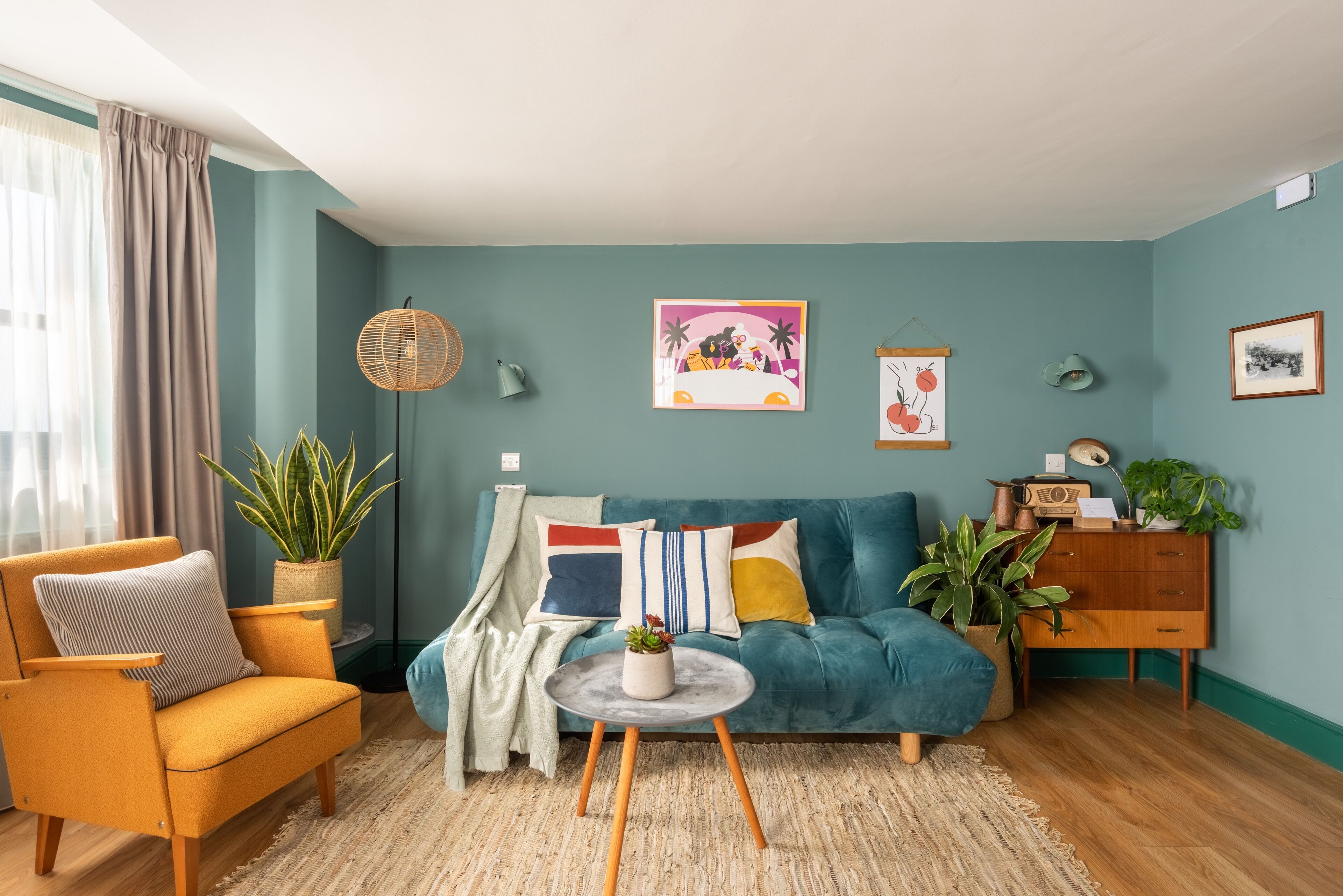 A living room with a teal sofa, a mustard armchair, and a round coffee table with a plant.