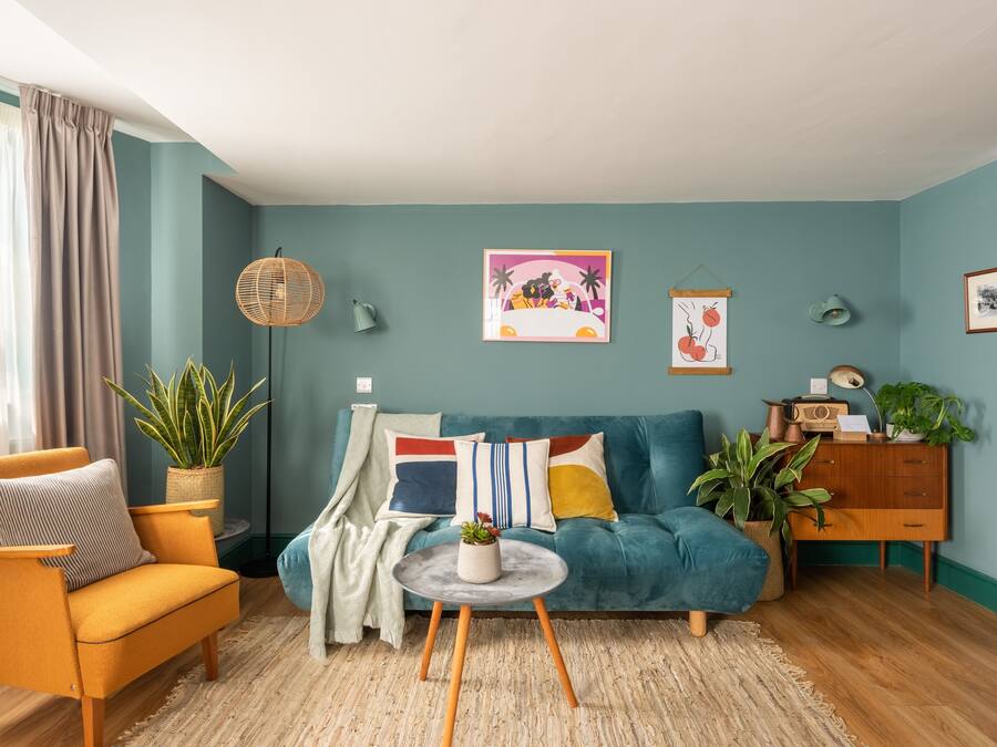 A living room with a teal sofa, a mustard armchair, and a round coffee table with a plant.