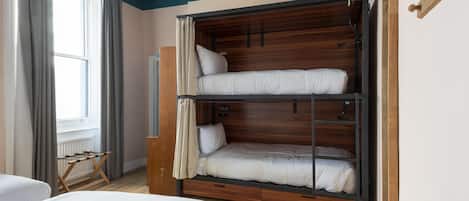 Quarto com beliche, janela com cortinas, piso de madeira e luminária suspensa.