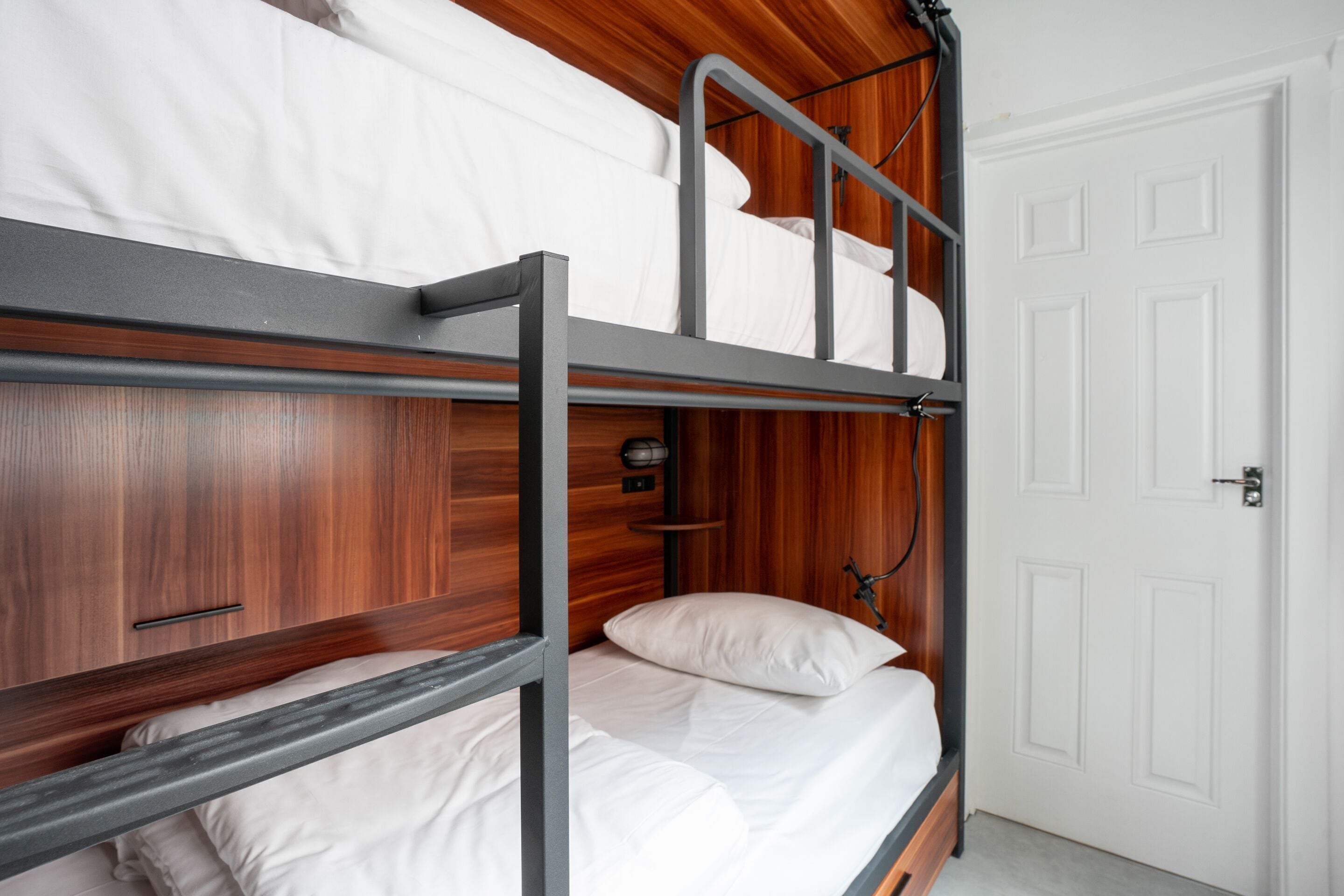 A bunk bed room with wooden paneling, a white door, and a small shelf with a lamp.