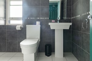 Un baño moderno con inodoro, lavamanos y cubo de basura.