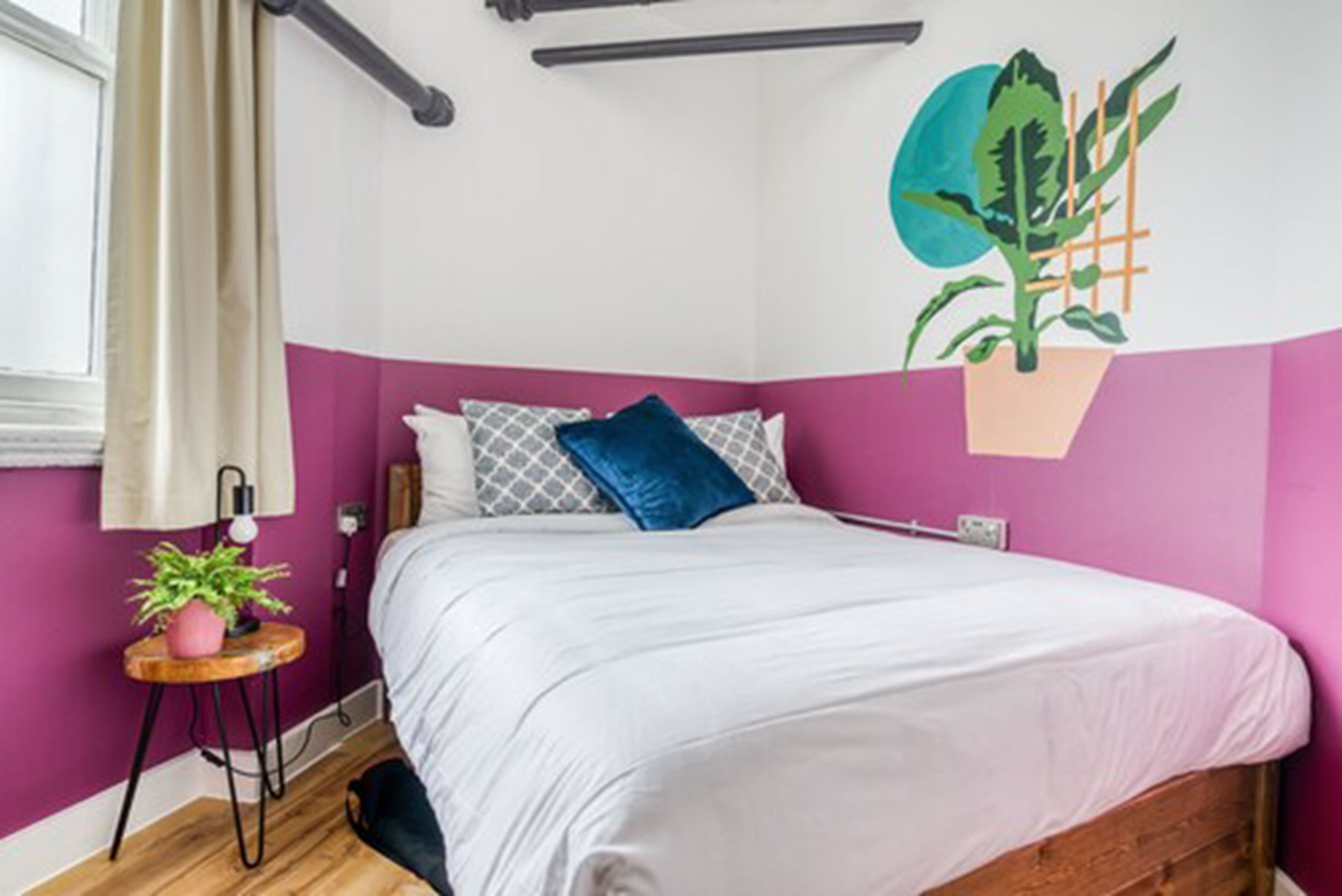 A bedroom with a bed, a potted plant, a lamp, and a wall decoration.