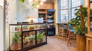 Een gezellig café met houten meubels, een glazen vitrine met planten en een koffieapparaat.