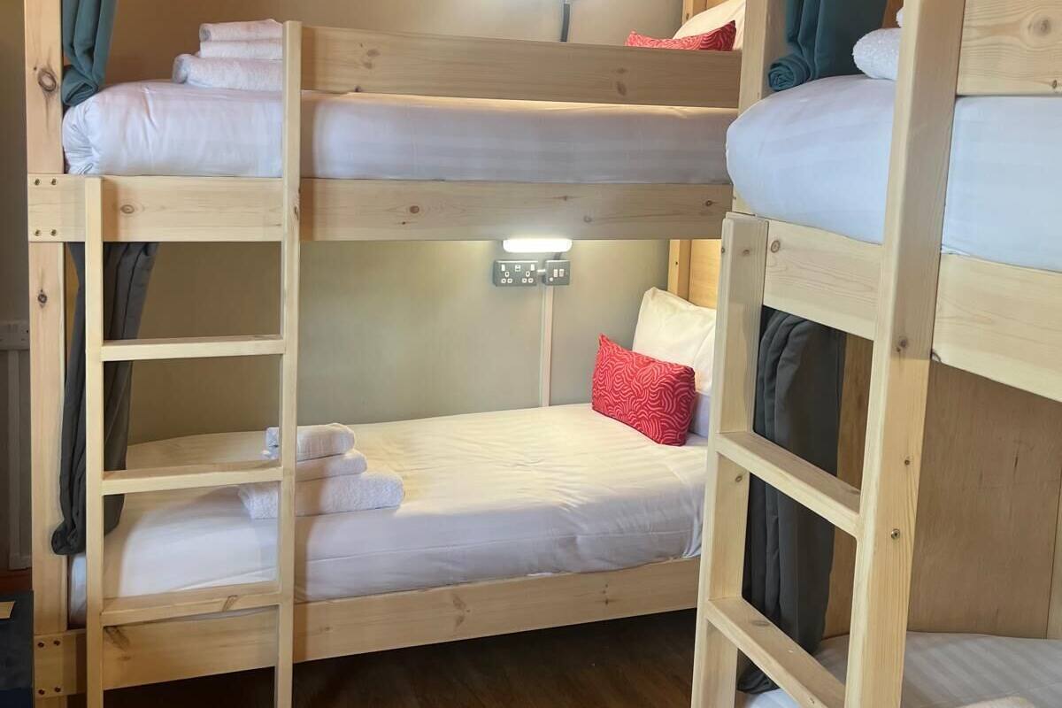 A bunk bed room with wooden frames, a bedside table, and a wall-mounted light.