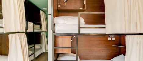 A dormitory-style room with bunk beds, wooden headboards, and curtains.