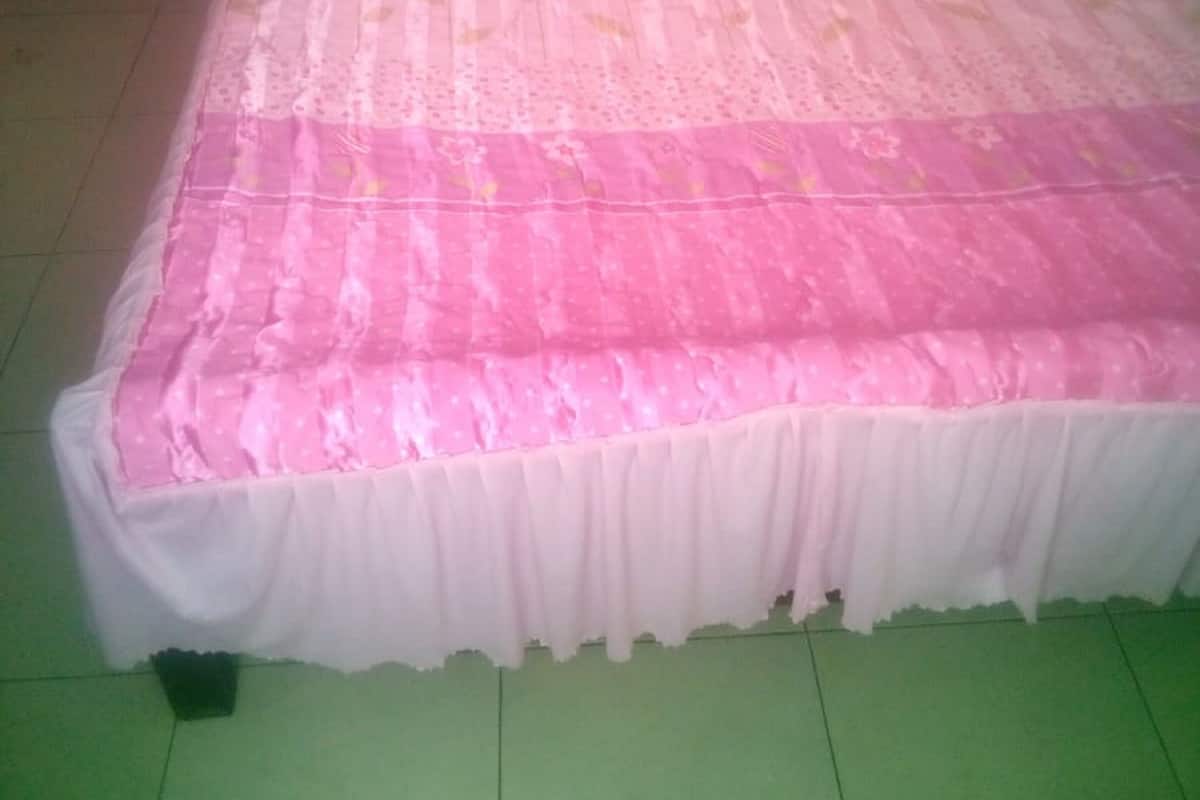Un lit avec une couvre-lit rose et blanche, une tête de lit en bois et une base recouverte d’une jupe blanche.