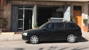 A two-story building with a black car parked in front. There are two visible windows on the ground floor and a door with a glass panel. - Appart Boutchakkat 3 (Agadir)