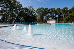 Une piscine dotée de jets d’eau, entourée d’arbres et de chaises longues.