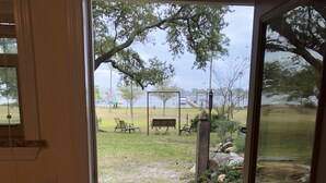 Une porte vitrée donne sur un patio équipé d’une balançoire, un petit jardin et offre une vue sur une étendue d’eau.